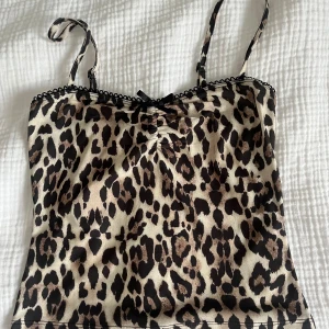 Leopardmönstrad linne med spetsdetalj - Snygg leopardmönstrad linne med tunna justerbara axelband och liten svart rosett framtill. Toppen har spetskant längs urringningen, aldrig använt!