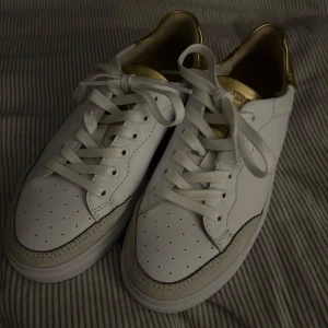 Sneakers - Ett par vita sneakers med en beige kant fram på skon och en guld detalj bak på skon. Från Ten Points, storlek 37. Helt nya, bara testade. Nypris 1895kr, de sista bilden.