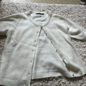 Helt ny vit kofta med pärlknappar från 157 - Supermjuk vit kofta från 157 med korta ärmar och rund hals. Jättegullig och oanvänd, min skola är väldigt kall därför har jag inte använt den. Sprillans ny och i perfekt skick