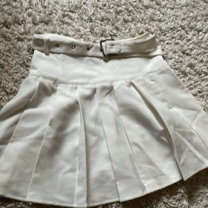 Vit plisserad kortkjol med bälte - Superfin vit kortkjol med matchande bälte med metallspänne som ger en snygg detalj. Gulligt och i bra skick, använts ett fåtal gånger, från Shein och pris går att diskuteras, inte min stil länge 