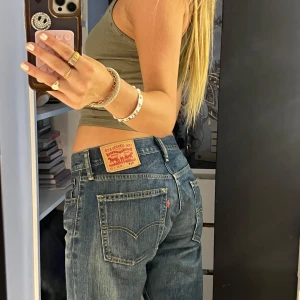 Levi's 514 blå jeans straight fit - Säljer ett par klassiska Levi's 514 jeans i blå denim. Modellen har rak passform, låg midja och snygga slitningar för en avslappnad vibe. Jeansen har fem fickor, gylf med dragkedja och tydliga kontrastsömmar. Perfekta för en cool och tidlös look.