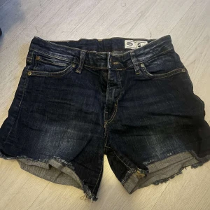Mörkblå jeansshorts från original  - Snygga mörkblå jeansshorts från original med råa, fransiga benslut och klassiska fem fickor. Shortsen har normal passform och tydliga kontrastsömmar. Perfekta för en chill sommarlook.