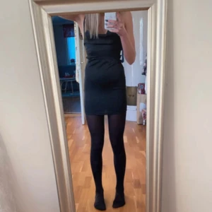 Svart kort klänning med snörning - Säljer en svart, tight kortklänning med smala axelband som korsas i ryggen och snygg snörning baktill. Klänningen är ärmlös och har en stilren, minimalistisk look som passar perfekt när du vill sticka ut. Materialet känns slätt och följsamt.