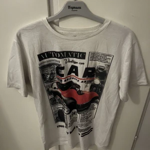 Vit t-shirt med vintage biltryck - Vit t-shirt med coolt vintageinspirerat tryck framtill som föreställer en röd sportbil och text i svart och rött. T-shirten har rund halsringning och korta ärmar. Perfekt för dig som gillar retro vibes och streetstyle.