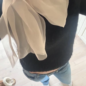 Svart stickad tröja med rosett - Supersöt svart stickad tröja med en stor beige vid axeln. Snygg detalj!