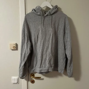 Grå hoodie från lager 157 i XL - Enkel och stilren grå hoodie från lager 157 i storlek XL. Tröjan har huva med snörning och är tillverkad i mjuk bomullsmix. Perfekt för chill dagar eller när du vill ha en avslappnad look. Katt finns i hemmet 