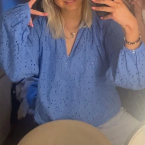 Blå broderad blus från H&M - Supersöt blå blus från H&M med broderade detaljer och hålmönster. Luftig modell med ballongärmar och v-ringning. Perfekt för vår och sommar, till jeans eller kjol. Tillverkad i bomull för en skön och lätt känsla.