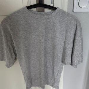 Ljusgrå	tajt vid magen, oversized/lösare ärmar - En ljusgrå t-shirt med korta stora ärmar och rund hals och tight runt magen vilket ger en slim och smickrande passform. T-shirten är i mjuk bomull. Perfekt inför hösten.🍁