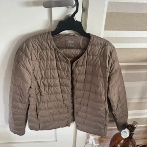 Beige dunjacka från Uniqlo, S - Lätt och smidig beige dunjacka från Uniqlo i storlek S. Jackan har rund halsringning, knäppning framtill och quiltad design. Perfekt för lager-på-lager och enkel att ta med sig. Snygg minimalistisk look som funkar till många outfits. Jätte fint skick 