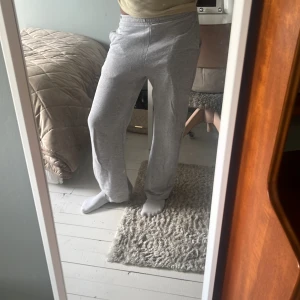 Grå mjukisbyxor - Säljer ett par grå mjukisbyxor från NYC med broderad logga framtill. Byxorna har elastisk midja och raka ben med loose fit, perfekta för chill dagar. Tillverkade i mjuk bomullsblandning för extra komfort.