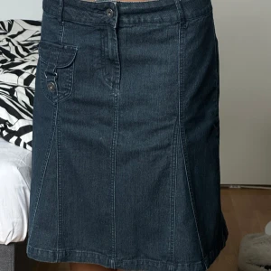 Mörk jeanskjol med fickdetalj - Snygg mörkblå jeanskjol med A-linjeform och cool ficka framtill med knapp. Kjolen har bälteshällor, dragkedja och knapp i midjan samt dekorativa sömmar. Perfekt för dig som gillar en klassisk men trendig denimlook.