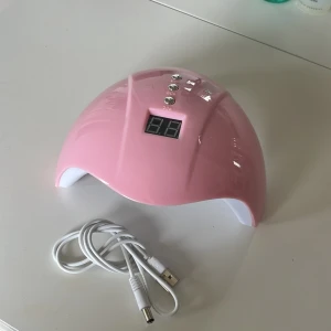 Rosa UV-lampa för naglar - Söt rosa UV-lampa med digital display och tre timerknappar (30s, 60s, 99s). Kommer med vit USB-sladd. Lampan har flera LED-lampor på insidan och är tillverkad i plast. Perfekt för att fixa gelnaglar hemma. Jag har knappt använt denna då jag har en annan. Jag vet inte vilket märke det är men tror den är från jultidningarna för flera år sedan. Inte bästa kvaliten men den funkar