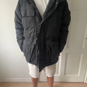 Grå parkas från The North Face - Säljer en mörkgrå parkas från The North Face med stor huva och snygg fuskpälsdetalj. Jackan har flera stora fickor framtill, dragsko i midjan och broderad logga på ärmen. Perfekt för kalla dagar och riktigt stilren look.