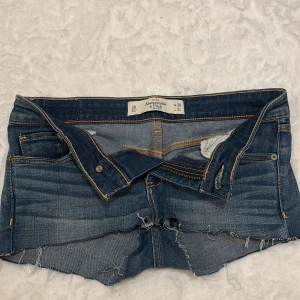Jeansshorts från Abercrombie & Fitch - Ett par lågmidjade blåa shorts från abercrombie & fitch. Ganska korta och har en tajt passform. Stretchiga ben och midja.