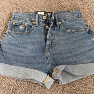 Blå högmidjade jeansshorts 157 - Klassiska blå jeansshorts från 157 med hög midja och uppvikta benslut. Shortsen har fem fickor, fyra knappar framtill.