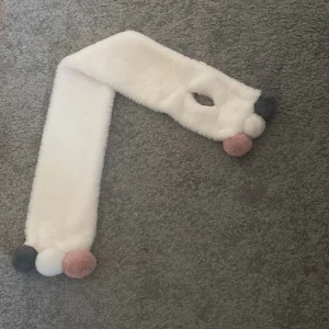 Vit halsduk med fluffiga bollar  - Fluffig halsduk med en öppning där man kan knyta statiken i. Det finns 3 st fluffiga bolar på kanten som är i 3 olika färger. Mycket skön när det börjar bli kallt ute 