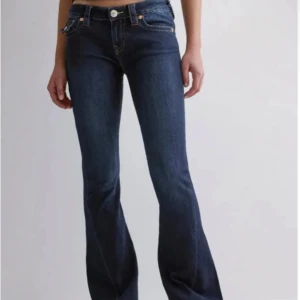 Mörkblå bootcut jeans True Religion - Snygga mörkblå jeans från True Religion med bootcut passform och klassiska kontrastsömmar. Byxorna har låg midja, markerade bakfickor med lock och knappar samt detaljerade sömmar. Perfekta för dig som gillar en tidlös men trendig look.