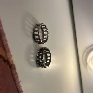 Två chunky silverringar med kedjemönster - Två coola silverfärgade ringar med chunky kedjedesign. En av ringarna har glittriga stenar längs ena sidan för extra bling. Perfekta för att ge din look en edgy vibe och passar lika bra till streetstyle som till mer dressade outfits.