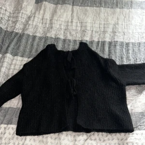 Svart stickad kofta från Gina Tricot - Mysig svart stickad kofta från Gina Tricot med långa ärmar och två knytband framtill. Koftan har en rak, lite croppad passform och är perfekt för lager-på-lager. Enkel och stilren design som funkar till allt. Storlek M men passar mig som är en S oxå 