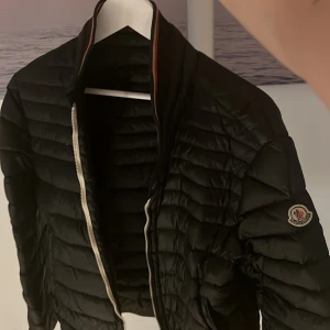Moncler jacka - Svart pufferjacka från Moncler som passar till vintern eller hösten, kanske till och med våren. Bra skick, 2 hål som man kan se på bild 4 & 5. Fast inget man märker vid användning. Annars är jackan i mycket bra skick. Äkta såklart. Mitt pris 500kr. Kontakta mig om du har frågor👍✅