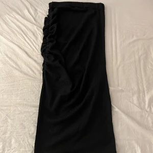 Svart långkjol med rynkade detaljer - Säljer en svart långkjol med snygg rynkning längs ena sidan. Kjolen har en rak passform och är perfekt för dig som gillar stilrena plagg med en twist. Enkel att matcha och passar året runt.