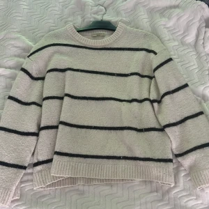 Randig stickad tröja från Gina Tricot - stickad tröja från Gina Tricot i ljusbeige med svarta horisontella ränder. Tröjan har rund halsringning, ribbade muddar.