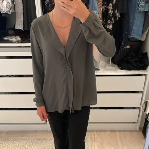 Mörk grön blus med v-ringning från Forever 21 - Super fin mörk grön blus från Forever 21 med v-ringad omlottkrage och långa ärmar. Blusen har en lös passform och knappar vid ärmsluten. Perfekt att styla med både jeans och kostymbyxor för en clean look. Blusen är mer grön i verkligheten!💚