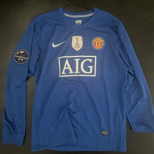 Manchester United Ronaldo 7 blå långärmad tröja - Blå långärmad Manchester United fotbollströja från Nike med Ronaldo 7 på ryggen. Champions 07/08-märke på ärmen, FIFA World Champions 2008-märke och AIG sponsortryck på bröstet. Broderat klubbmärke och Nike-logga. Tillverkad i lätt och ventilerande material.