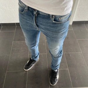 Tiger Of Sweden Jeans - Säljer ett par blå skinny jeans från Tiger Of Sweden i storlek 31/34. Jeansen har klassisk femficksdesign, snygga slitningar och orangea sömmar. Tillverkade i mjukt denimtyg som sitter tight och följer kroppen. Perfekta för dig som gillar en modern och smal siluett.