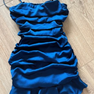 Blå satin kortklänning från Parallel Lines - Supersnygg blå kortklänning från Parallel Lines i glansig satin med rynkade detaljer och smala axelband. Klänningen har en figurnära passform och dragkedja i sidan. Använd 1 gång. Storlek 12 men passar mycket mer som s/m eller 38/40. Färgen är lugnare i verkligheten