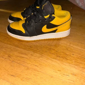 Nike Air Jordan 1 Low svart/gul - Säljer ett par Nike Air Jordan 1 Low i svart och gul. Skorna har klassisk Jordan-logga på hälen, svart snörning och vit sula. Ovandelen är i skinn med kontrasterande färgblock och ikonisk Swoosh i gult på sidan. Perfekta för dig som vill sticka ut med en fet färgkombo.