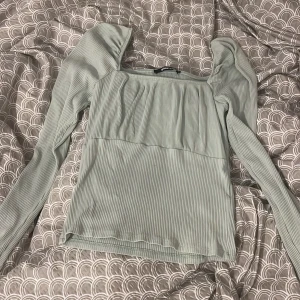 Ljusgrön ribbad topp Gina Tricot - Supersöt ljusgrön ribbad topp från Gina Tricot med långa ärmar och fyrkantig urringning. Toppen har en lätt puffig axel och är figurnära i modellen, perfekt för dig som gillar en stilren men trendig look.