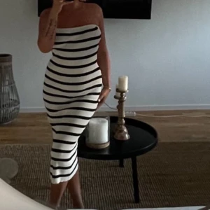 Randig axelbandslös klänning  - Snygg axelbandslös klänning med svartvita horisontella ränder. Klänningen är figurnära och går ner till vaden, perfekt för dig som gillar en tight och stilren look. Materialet känns mjukt och stretchigt, men är ändå väldigt rubust samtidigt för att formerna ska va där dem är, vilket gör den bekväm att bära hela dagen. Ansvönd vid 1 tillfälle 