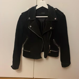 Svart bikerjacka från Vero Moda - Snygg svart bikerjacka från Vero Moda med coola silvriga dragkedjor och detaljer. Jackan har klassisk krage, axelklaffar och är tillverkad i mockaliknande material. Perfekt för dig som vill ha en edgy look med stilrena vibbar.