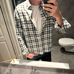 Rutig oxfordskjorta från GANT - Säljer en klassisk rutig oxfordskjorta från GANT i svart och vitt. Skjortan har normal passform, långa ärmar och knappar framtill. Perfekt för dig som gillar en tidlös och avslappnad stil. Tillverkad i bomull för skön känsla hela dagen. NYPRIS: 1400kr