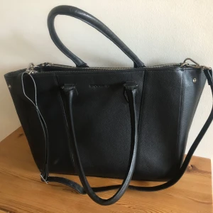 Svart handväska i skinn från Stockholm Leia serien - Snygg svart handväska i äkta skinn från Stockholm med stilren design. Väskan har både handtag och axelrem, dragkedja upptill och flera innerfack för smart förvaring samt knapplås.  Perfekt storlek för att få plats med allt du behöver till vardagen. Nypris 1599kr. Inköpt 2022. Jättefint skick! Mått: bredd 36cm, höjd 29cm. 
