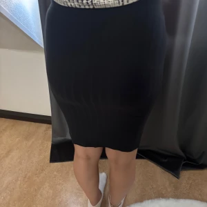 Svart tight kjol i stretchigt tyg - En svart, figurnära kjol i stretchigt material som sitter snyggt och markerar siluetten. Kjolen är knälång och har en enkel, stilren design utan synliga detaljer. Perfekt för dig som gillar en clean och klassisk look.