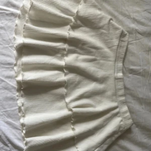 Vit volangkjol i bomull - Supersöt vit kortkjol med volanger och bred resår i midjan. Kjolen är gjord i ett mjukt bomullstyg och har en luftig känsla, perfekt för varma dagar. Enkel att matcha med crop tops eller stickade tröjor.