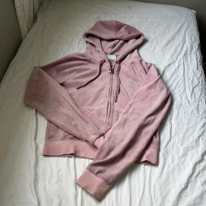 Rosa Juicy Couture hoodie - Superfin rosa hoodie från Juicy Couture i mjuk velour med glittrande strasstenar på bröstet och stor 'Juicy'-text på ryggen. Tröjan har huva, dragkedja och snörning med metalländar. 