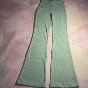 Ribbade gröna bootcut-byxor Divided - Snygga ljusgröna ribbade bootcut-byxor från Divided by H&M. Byxorna har hög midja, stretchigt material och vida ben. Perfekta för dig som gillar en trendig och bekväm look. Storlek XXS.
