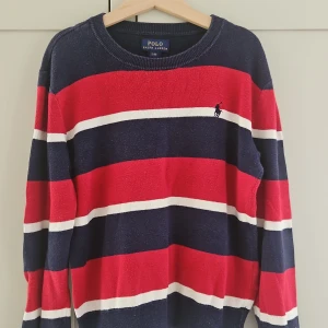 Randig tröja från Polo Ralph Lauren - Snygg randig tröja från Polo Ralph Lauren i marinblått, rött och vitt. Klassisk rund halsringning och långärmad modell med broderad logga på bröstet. Perfekt för dig som gillar preppy stil och vill sticka ut med färg. Materialet är mjukt och skönt.
