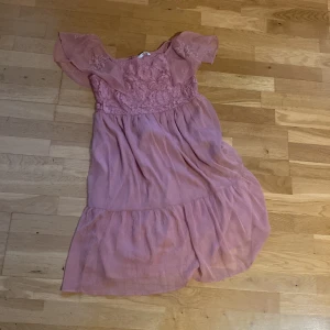 Rosa spetsklänning från Ellos - Supersöt rosa klänning från Ellos med volangkjol och korta ärmar. Överdelen har vacker spets och dragkedja i ryggen. Perfekt för dig som gillar romantisk stil och vill sticka ut lite extra.