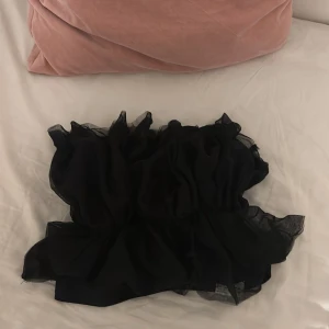Fest topp svart volanger  - Passande till nyår! Supersnygg svart tubtopp med volanger. Toppen är axelbandslös och har en cool, puffig look som verkligen sticker ut. Perfekt för dig som vill ha något unikt och trendigt. Använd en gång