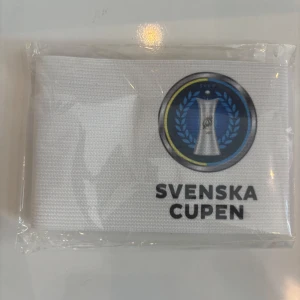 Vit kaptensbindel Svenska Cupen - Vit elastisk kaptensbindel med Svenska Cupen-logga framtill. Bindeln har kardborrestängning för enkel användning och sitter bekvämt runt huvudet eller armen. Perfekt accessoar för fotbollslaget och matcher.