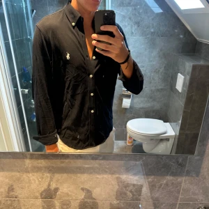 Marinblå skjorta Polo Ralph Lauren S - Svart skjorta från Polo Ralph Lauren i lätt mesh-bomull. Klassisk passform med vita knappar och broderad logga på bröstet. Långärmad och med button down-krage, perfekt för en clean och stilren look.