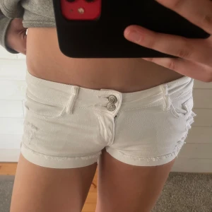 Vita lågmidjade jeansshorts från Tally Weijl - Snygga vita jeansshorts från Tally Weijl med låg midja och fransiga kanter. Shortsen har slitna detaljer, fem fickor och dubbla knappar framtill. Perfekta för sommaren och ger en fräsch look till din outfit. 