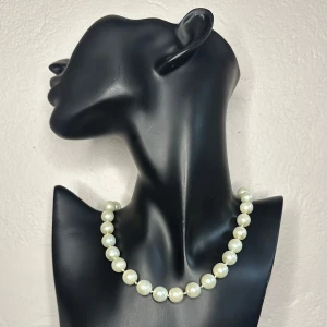 Vintage pärlhalsband – Klassisk Hollywoodglamour från 50-tal/60-tal - Tidlöst vintagehalsband från sent 50-/tidigt 60-tal med stora, krämvita imitationspärlor (ca 1 cm), knutna på tråd. Ca 47 cm, justerbar längd med charmig låsdetalj. Stilren midcentury-design i klassisk Hollywoodanda – perfekt till retroklänning eller som kontrast till modern look. Längd: ca 47 cm. Prutning accepteras ej, men jag erbjuder bundlerabatt. Jag rensar smyckesskrin och garderob – kika gärna på mina andra annonser!  ⸻  