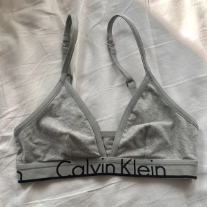 Grå linnetopp från Calvin Klein - Snygg grå linnetopp från Calvin Klein med justerbara axelband och bred resår med logga under bysten. Tillverkad i mjuk bomullsmix med elastan för extra komfort. Perfekt för en chill och sportig look.