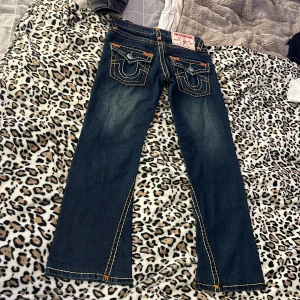 True Religion jeans med kontrastsömmar - Mörkblå jeans från True Religion med ikoniska kontrastsömmar i orange och gul, dragkedjan är sönder men kan nog fixas 