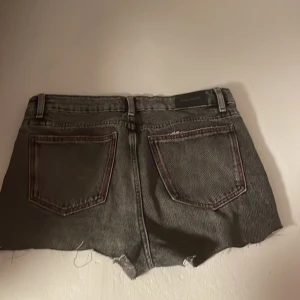 Svarta jeansshorts med slitningar - Det är avklippta jeans från Gina Tricot, använt 1-2 gånger. Säljer pga försmå. Dem sitter lite under naveln men man kan även vika ner dom. Dem har en rosa knapp och rosa bandet på bakfickorna.